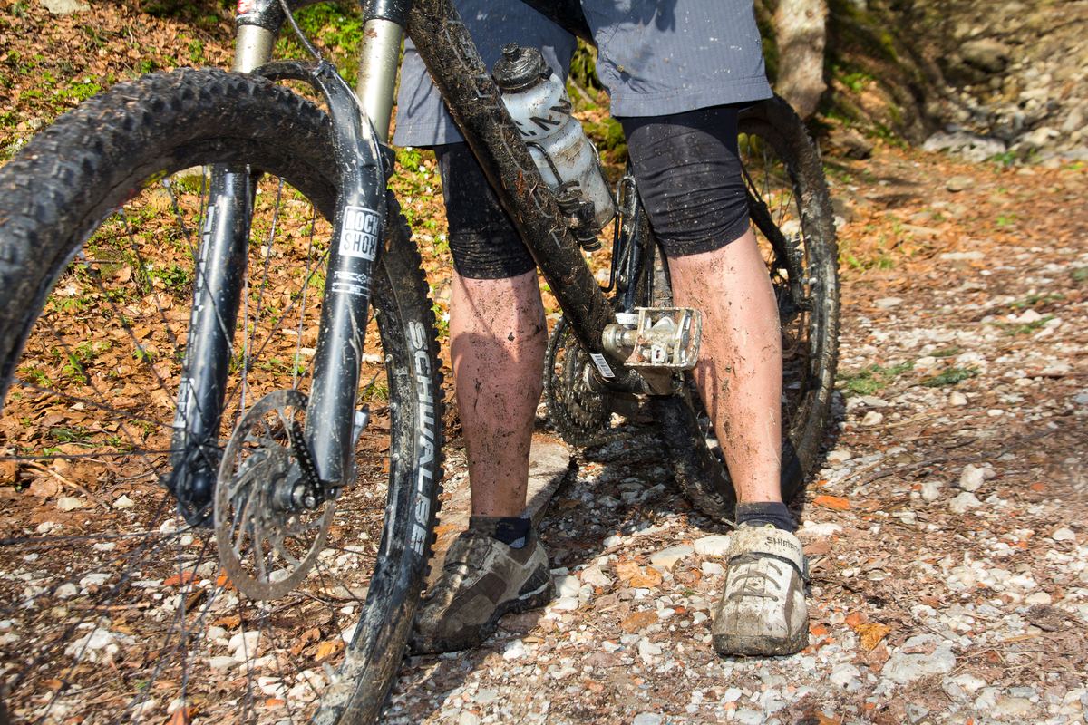 Matschige Beine und ein schlammverschmiertes Mountainbike auf einem Waldweg